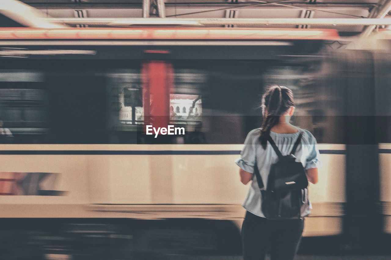 Rear view of woman standing by blurred train at railroad station