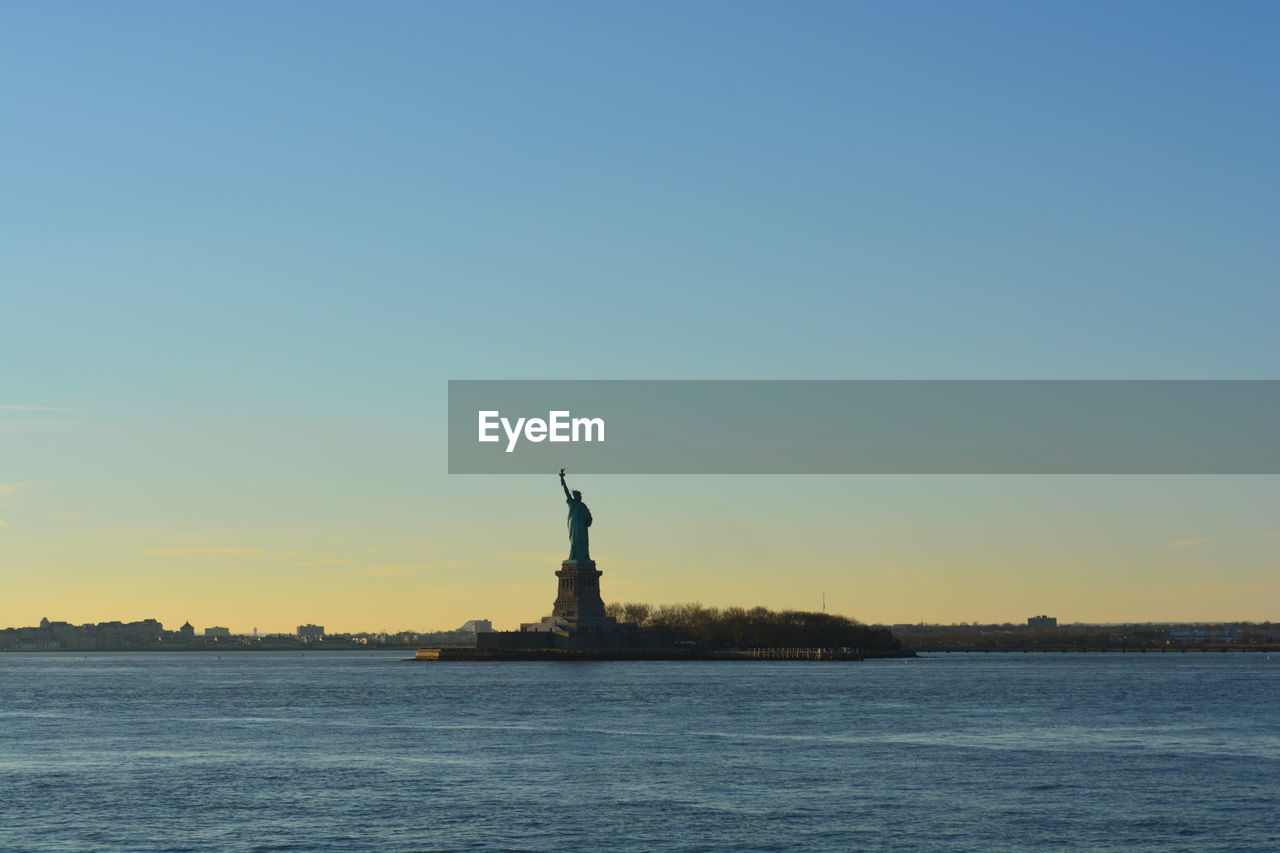 Statue of liberty by hudson river against clear sky during sunset