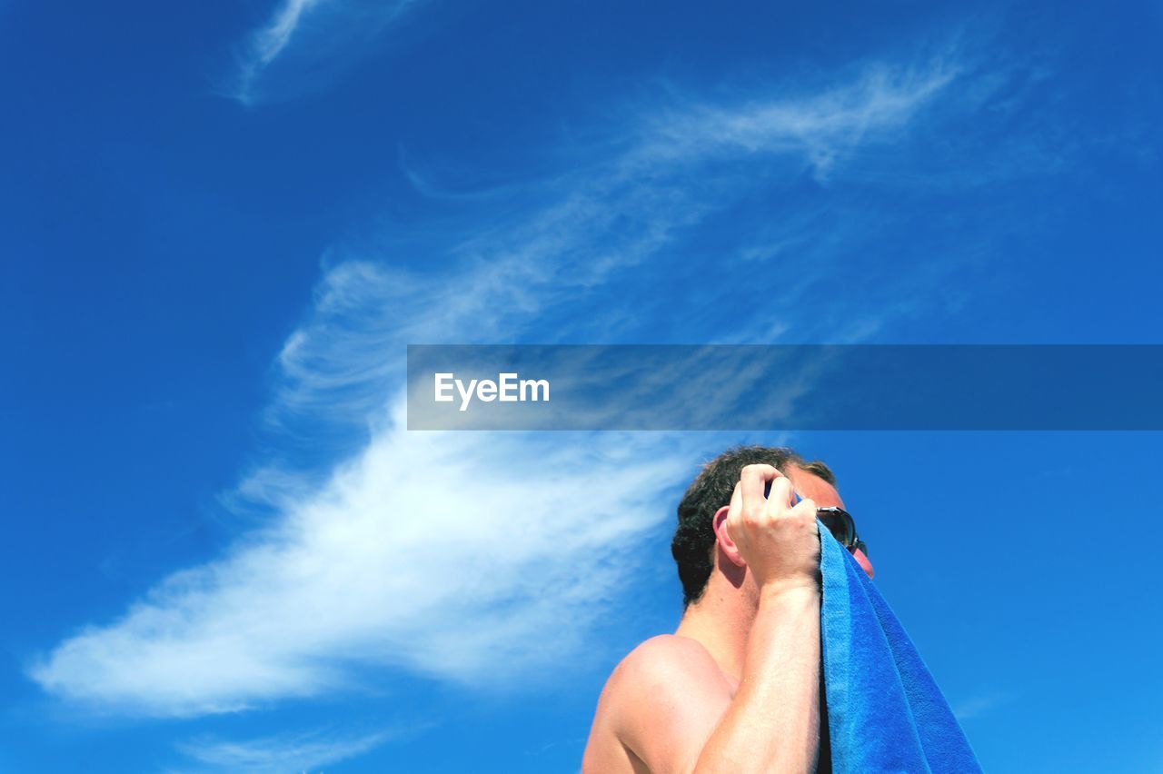 LOW ANGLE VIEW OF WOMAN STANDING AGAINST BLUE SKY