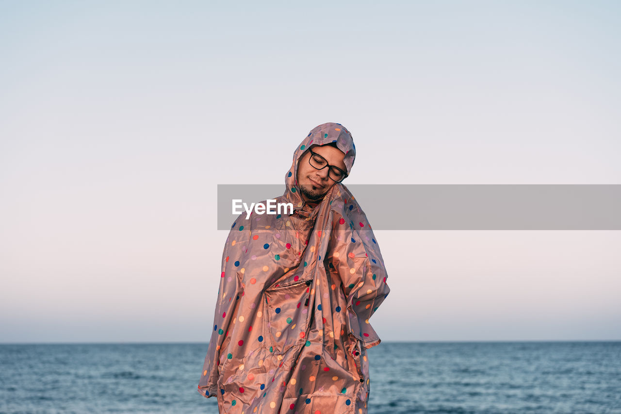 Person standing in raincoat by sea against clear sky