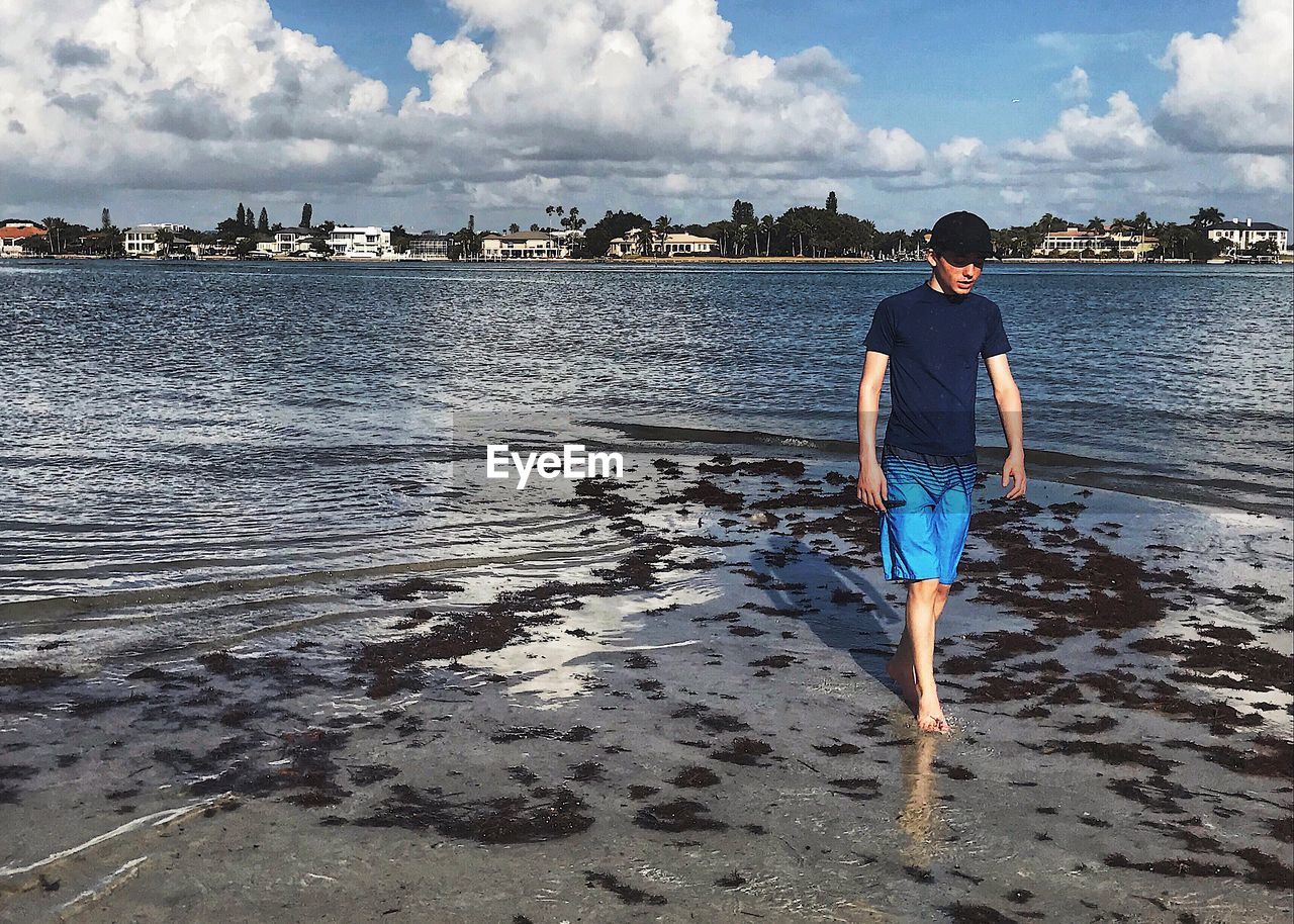 Teenage boy walking at beach against sky