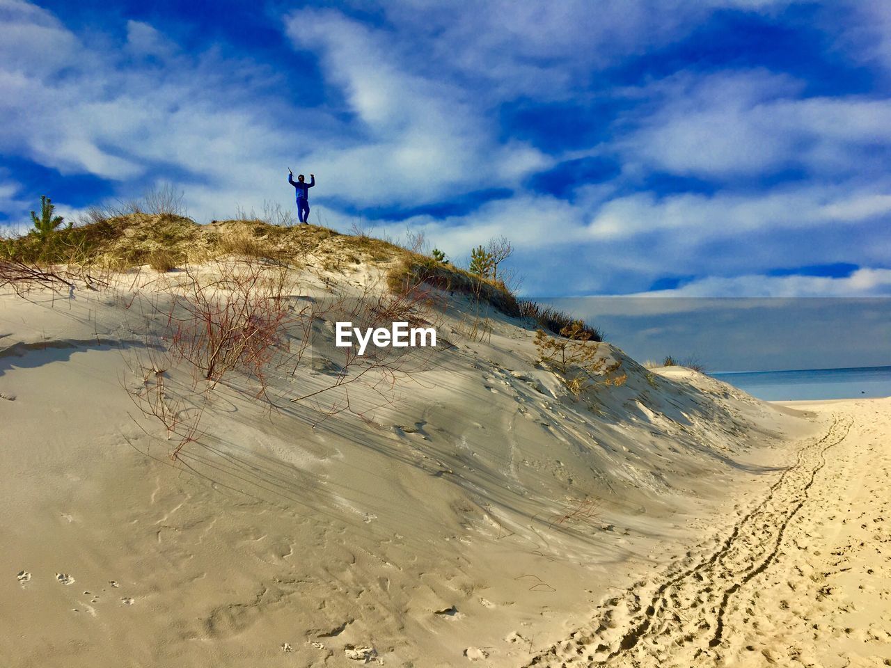 Low angle view of man standing on sandy hill against cloudy blue sky