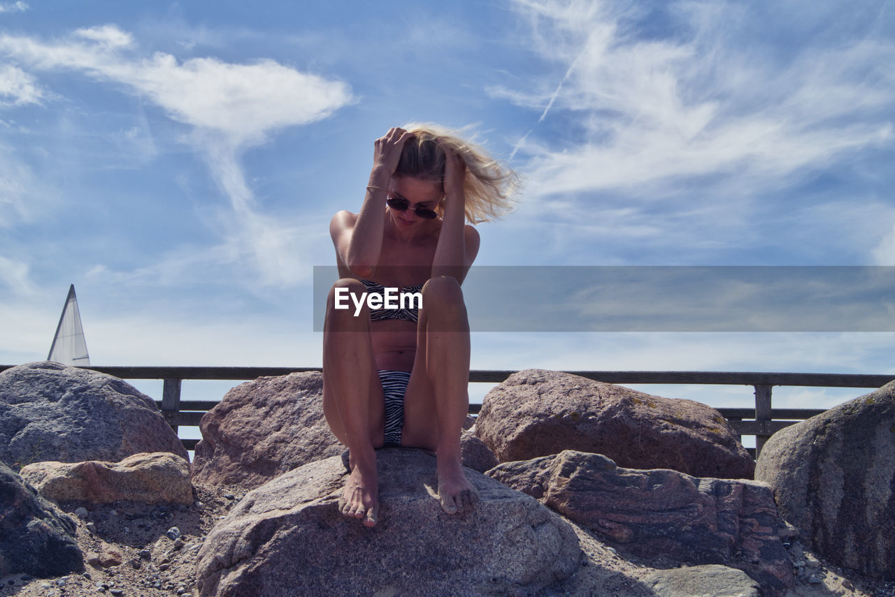 Full length of woman sitting on rock against sky