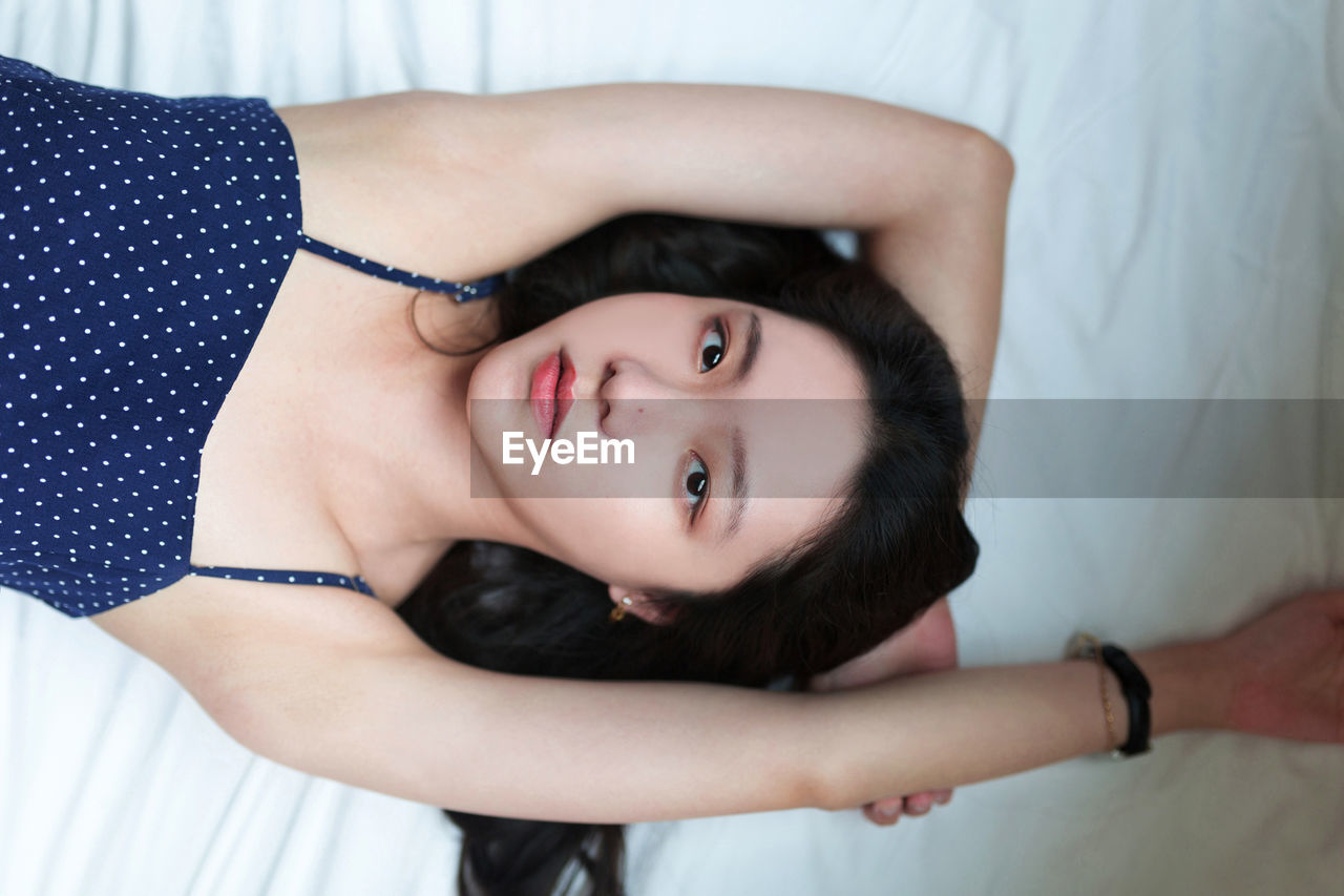 High angle portrait of young woman lying on bed