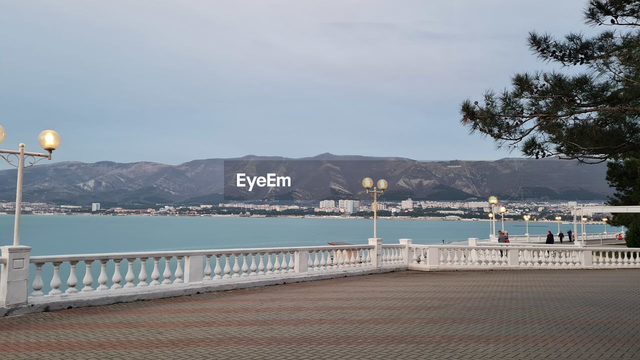 water, sky, mountain, architecture, sea, nature, walkway, travel destinations, street light, built structure, scenics - nature, transportation, railing, travel, city, vacation, beach, land, beauty in nature, tourism, day, boardwalk, tree, street, lighting equipment, coast, no people, mountain range, outdoors, building exterior, pier, tranquility, holiday, cloud, tranquil scene, trip, plant, nautical vessel, footpath