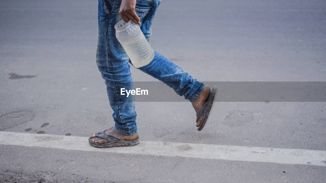Low section of man carrying water in plastic bottle while walking on road
