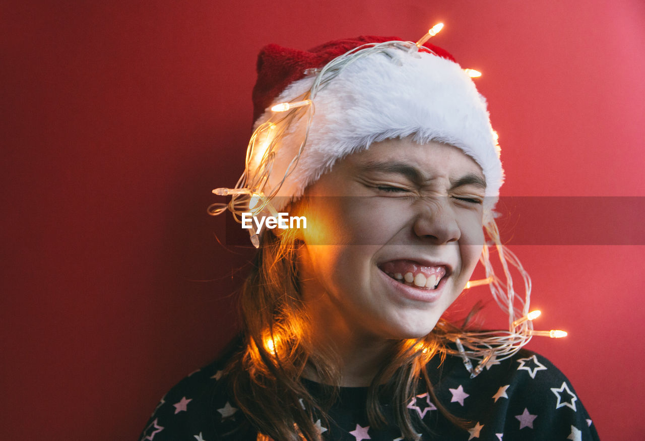 Girl with illuminated string light against red wall