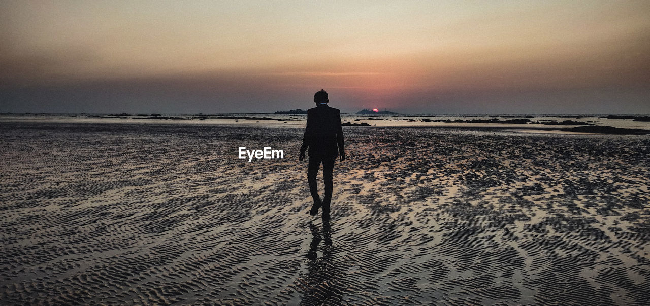 Rear view of man walking on a beach during sunset, towards oblivion.