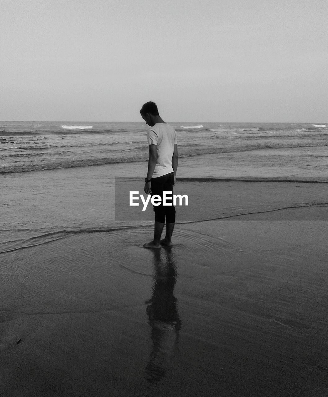 Man standing on shore at beach against clear sky