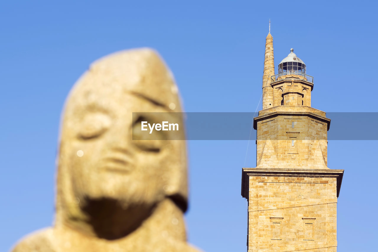 Tower of hercules and statue against clear blue sky