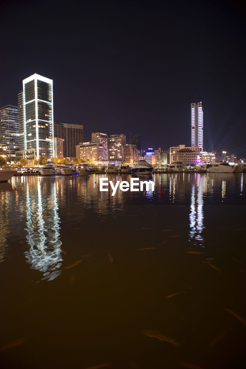 ILLUMINATED BUILDINGS BY RIVER AGAINST SKY