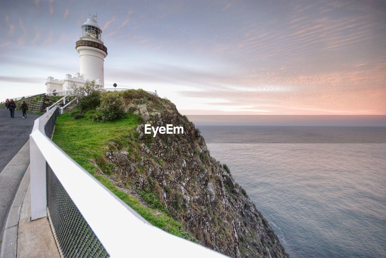 Lighthouse by sea against sky during sunset