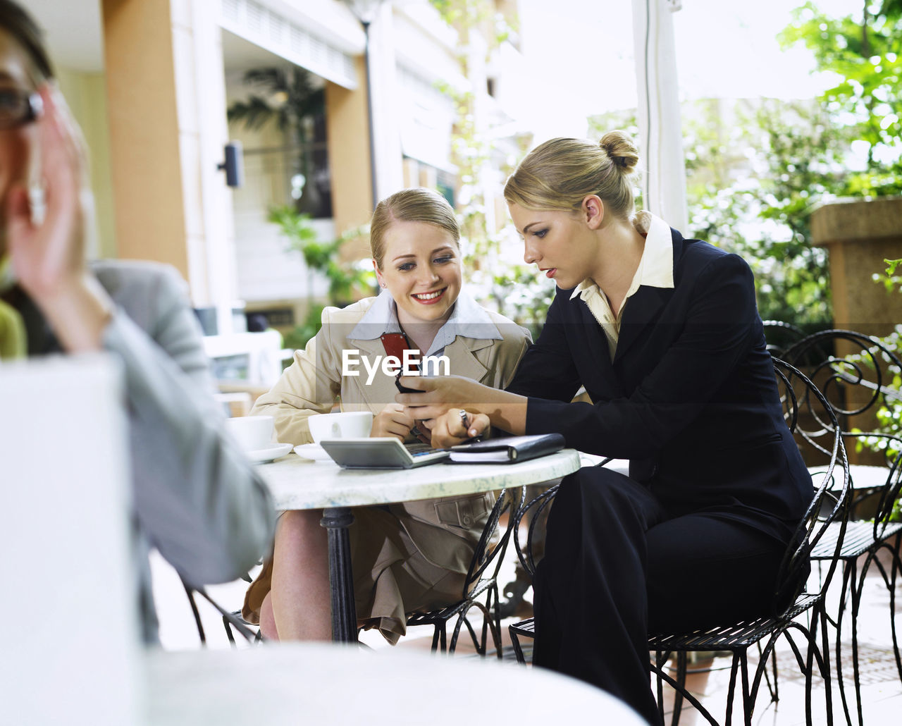 Businesswoman with colleague using phone at cafe