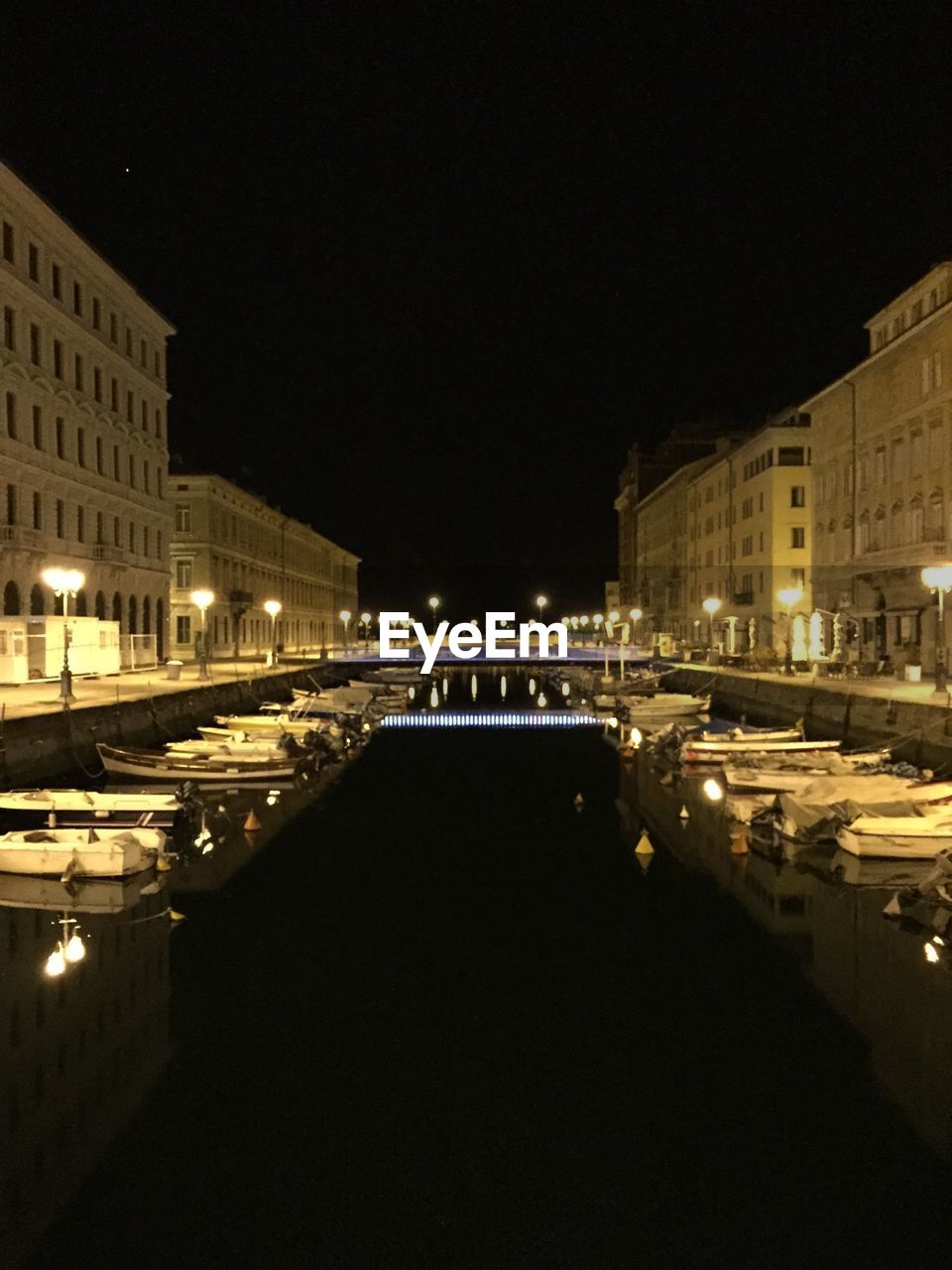 Boats moored in canal along buildings at night