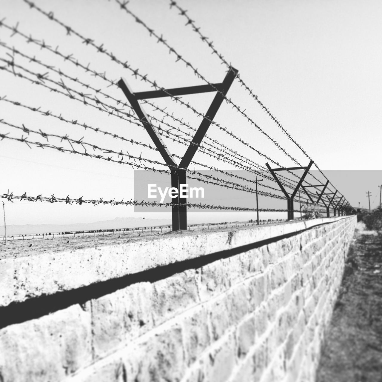 Barbed wire fence on retaining wall against sky