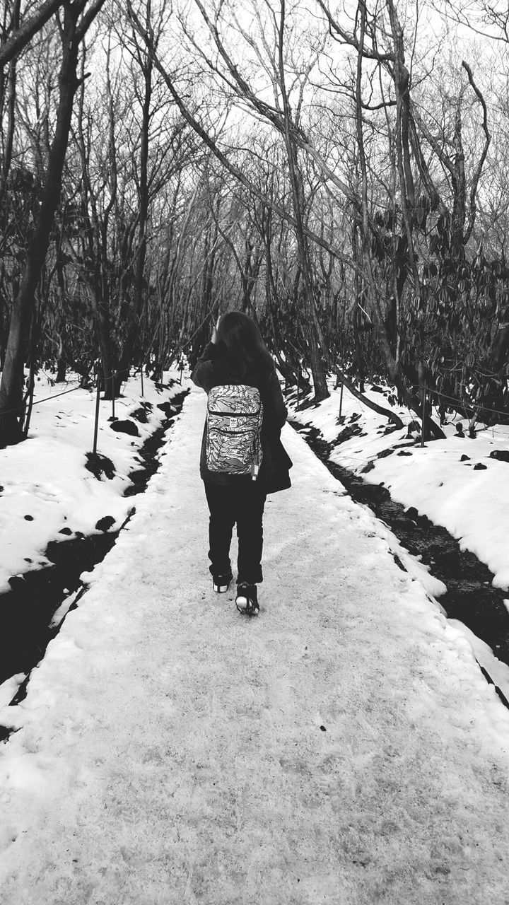 Rear view of woman with backpack walking on snow covered road amidst bare trees