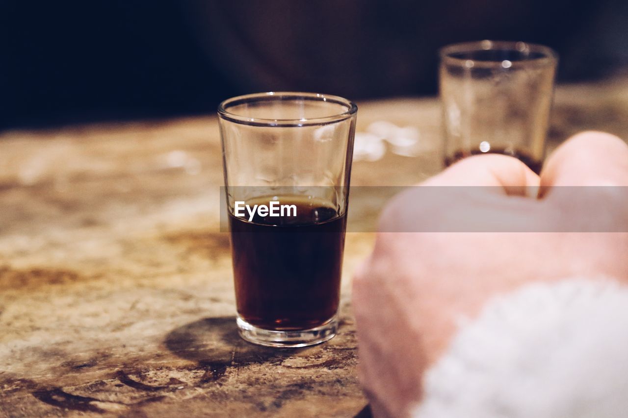 Close-up of hand beside a glass of sherry on wooden shelf 