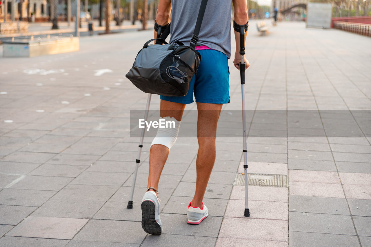 Unrecognizable young man with crutches walking in the city