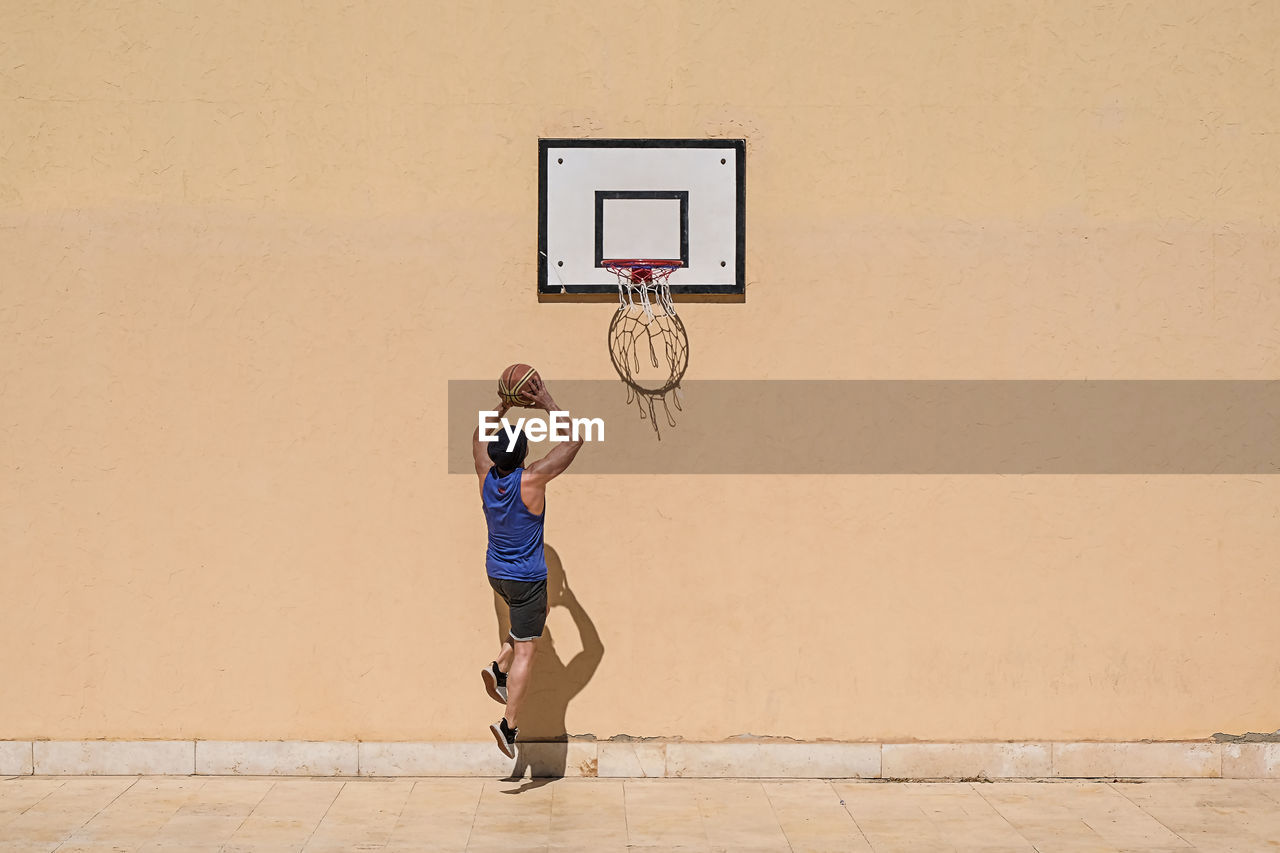 Man playing with basketball against beige wall