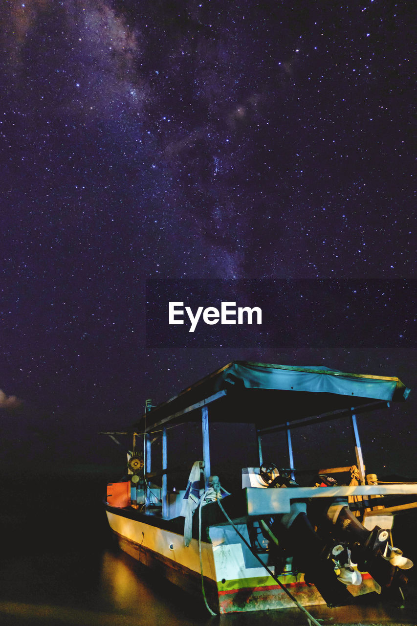 BOATS MOORED AT NIGHT AGAINST SKY