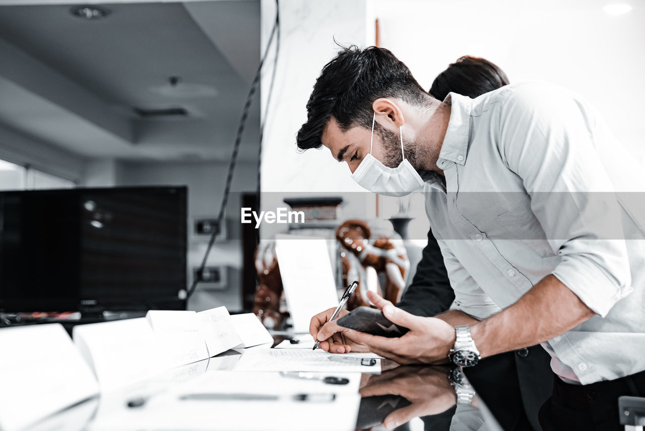 Young man wearing mask writing in office