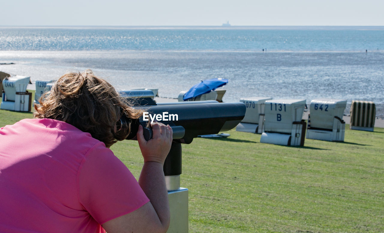 Woman looking at sea through binoculars on field