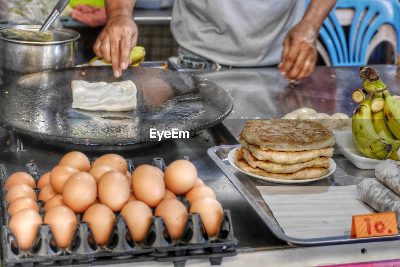 MIDSECTION OF MAN PREPARING FOOD IN KITCHEN AT MARKET