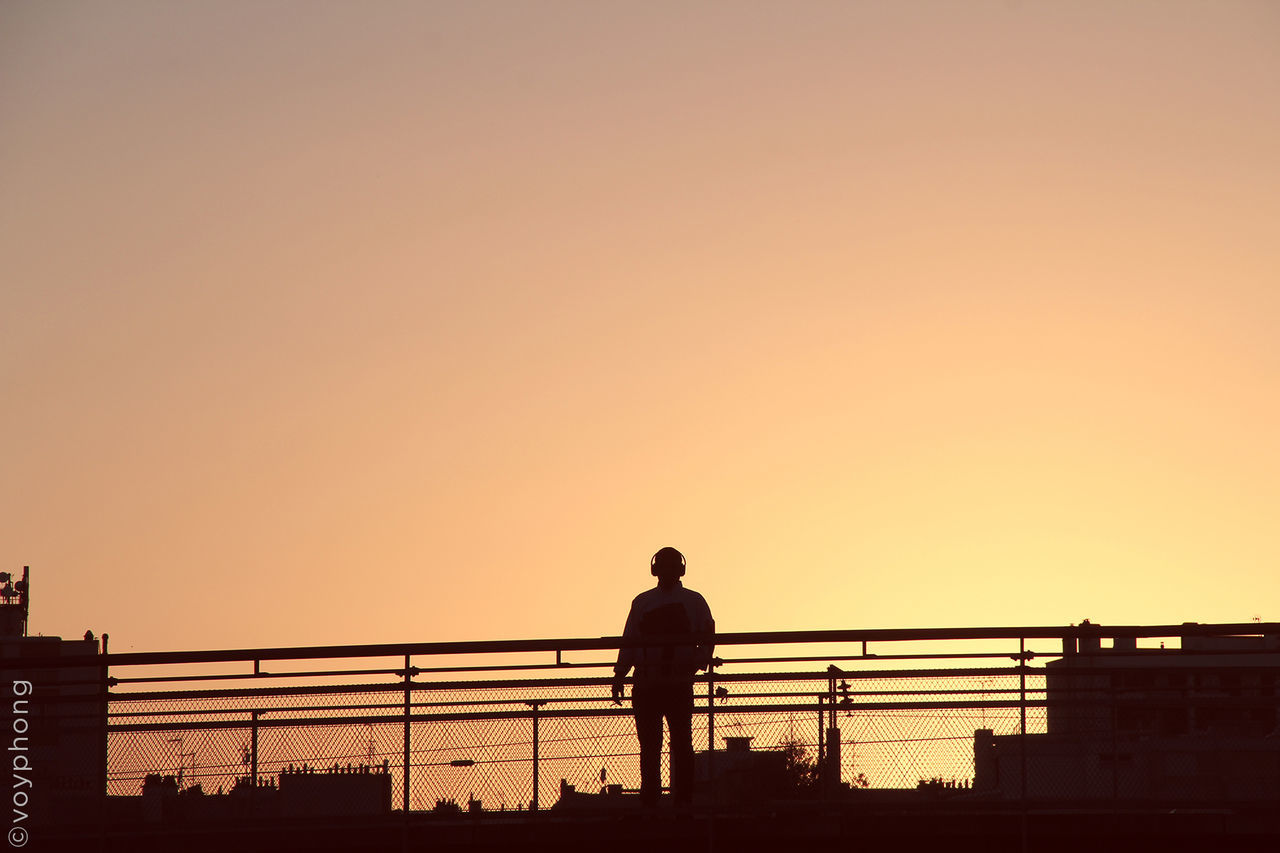 Rear view of silhouette man standing against orange sky at sunset