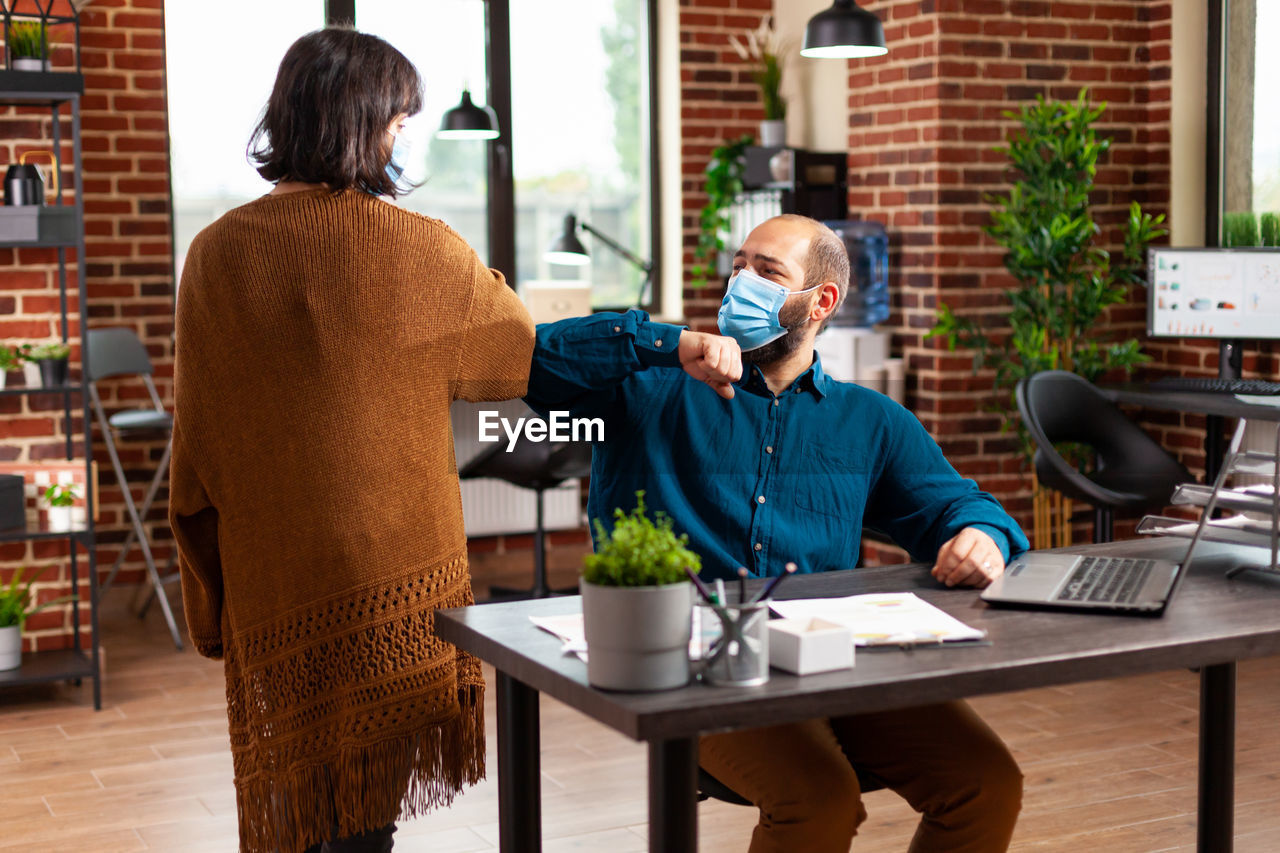 Business people wearing mask bumping elbow at office