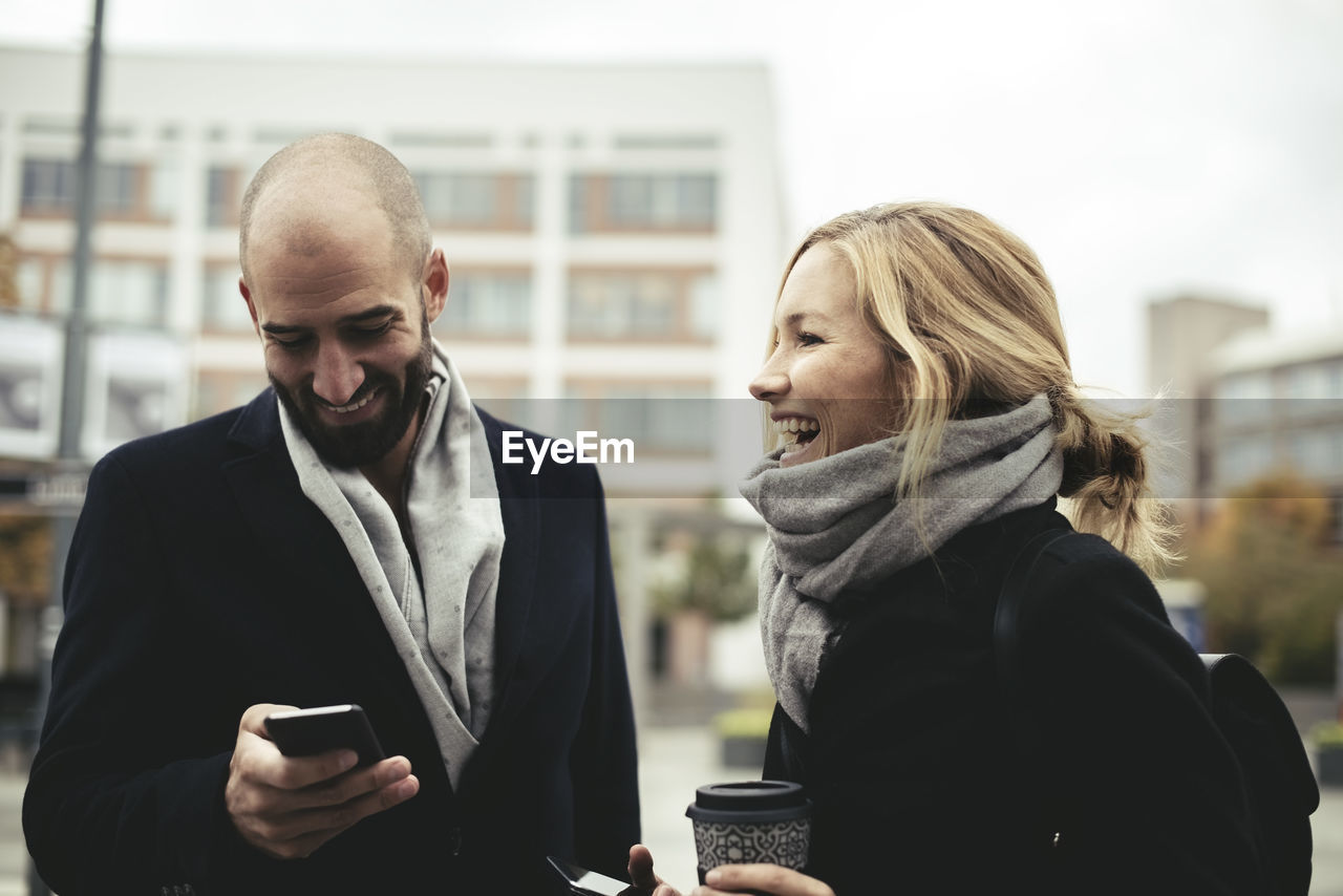 Smiling business people holding smart phones on sidewalk in city