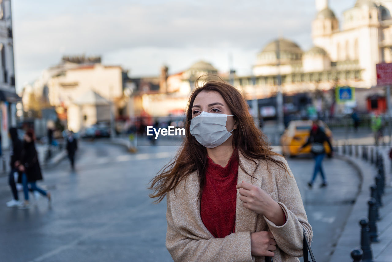 Woman wearing mask looking away standing on street