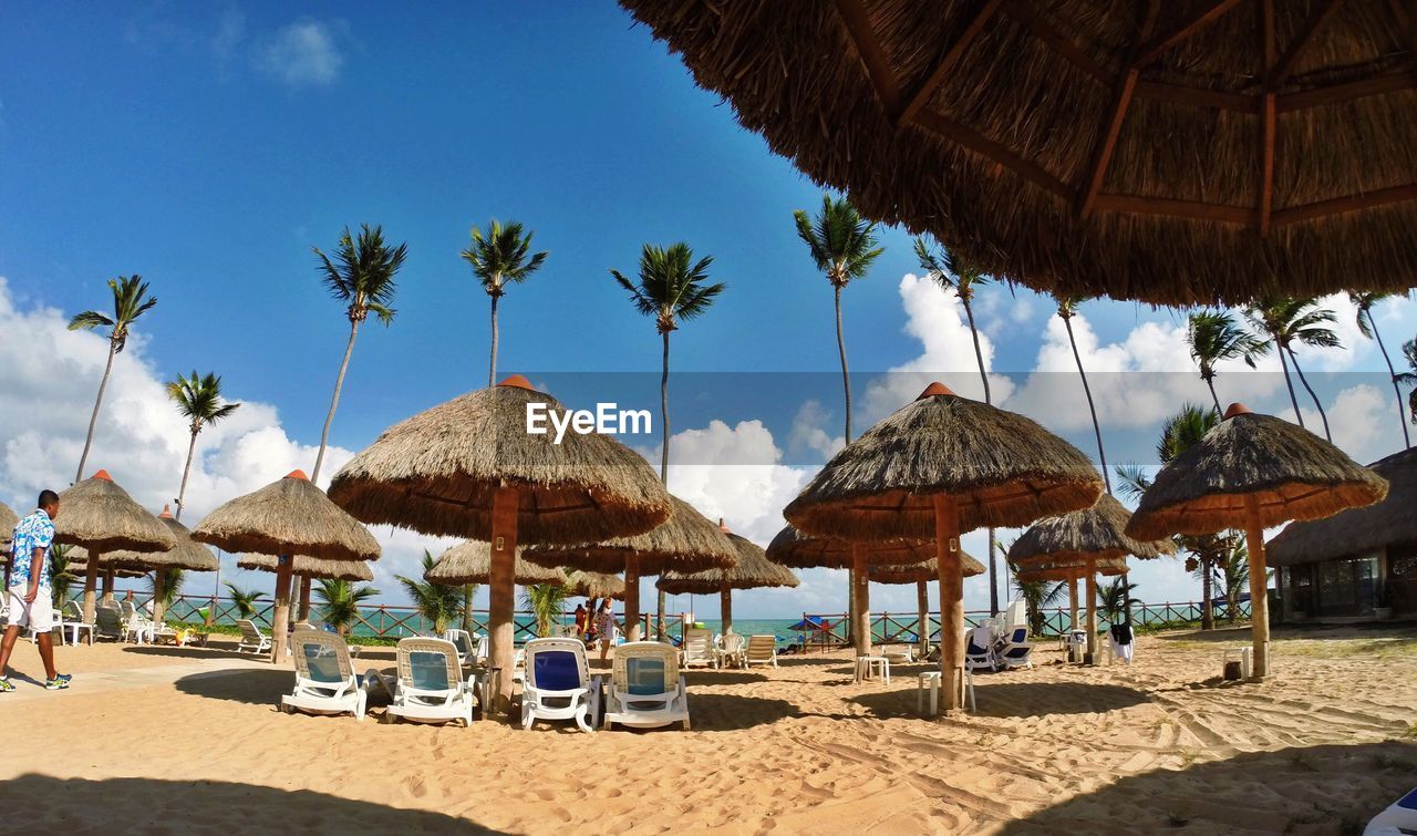 Lounge chairs and umbrellas on beach against blue sky