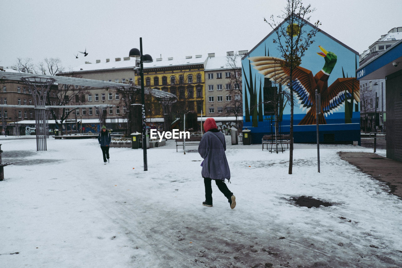 REAR VIEW OF MAN WALKING ON SNOW COVERED CITY