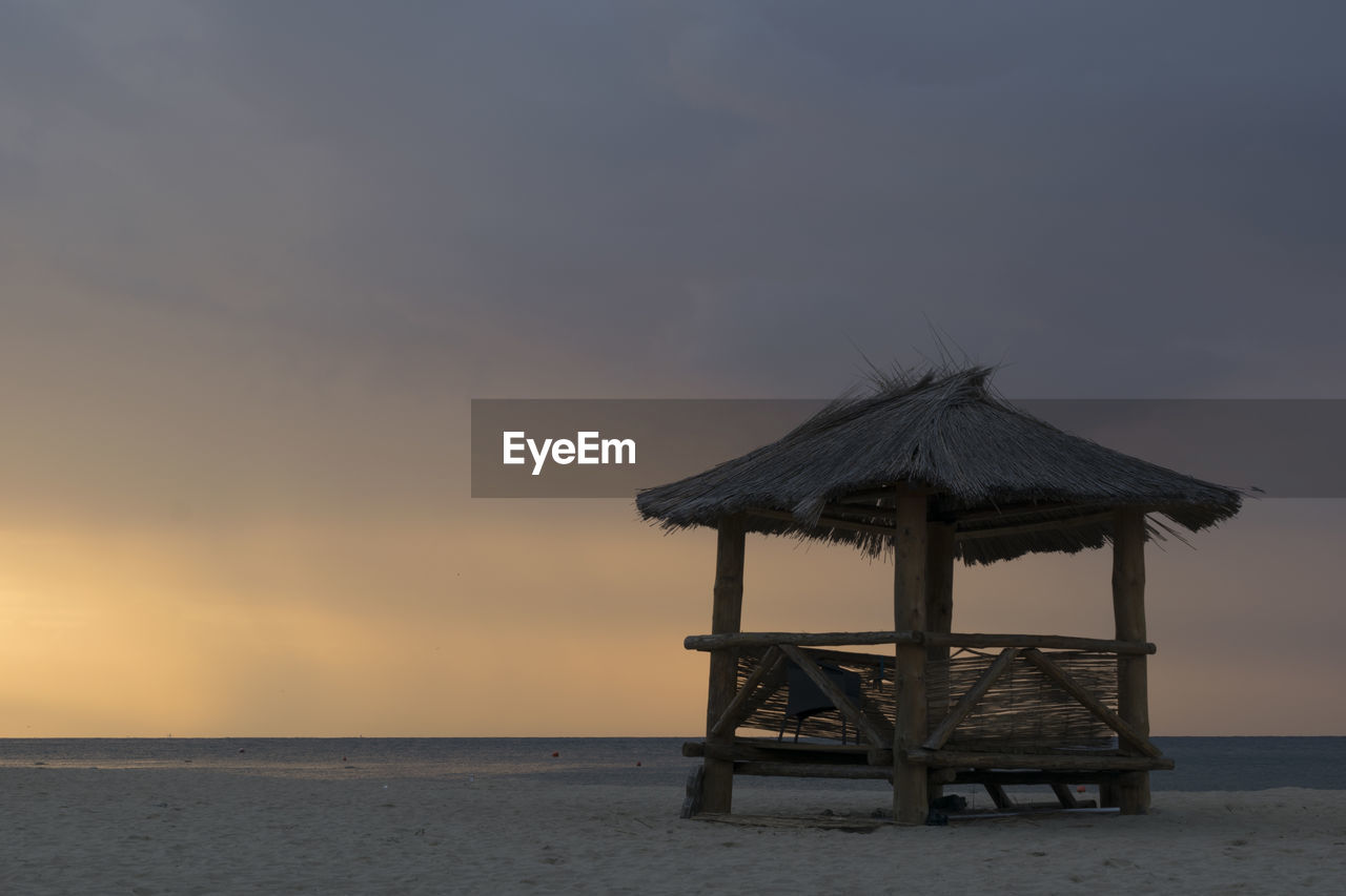 GAZEBO ON BEACH AGAINST SKY AT SUNSET