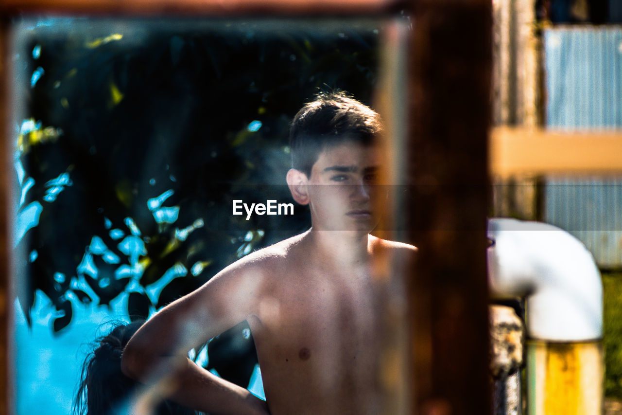 Portrait of shirtless young man reflecting on mirror