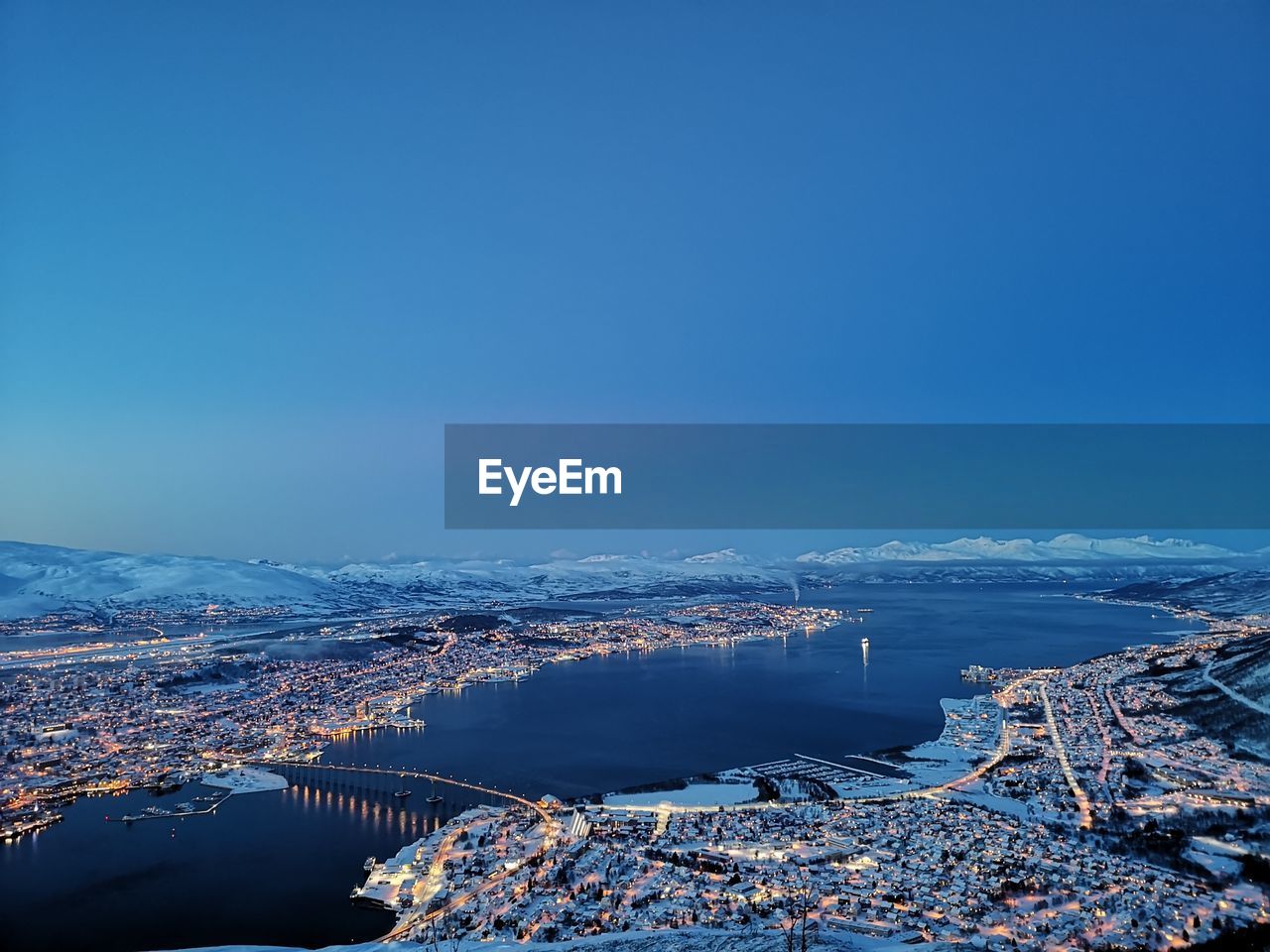 High angle view of city by sea against clear blue sky