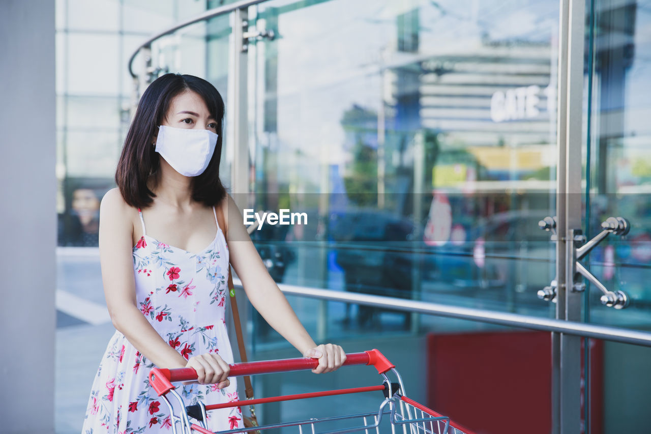 Asian woman wearing face mask with chopping cart lining up to wait for shopping