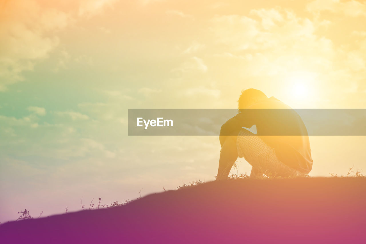 Side view of man sitting on land against sky during sunset