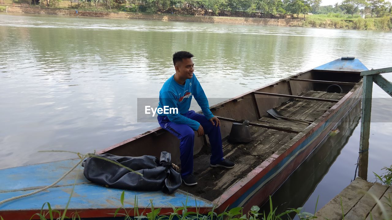 YOUNG MAN SITTING ON BOAT AT LAKE