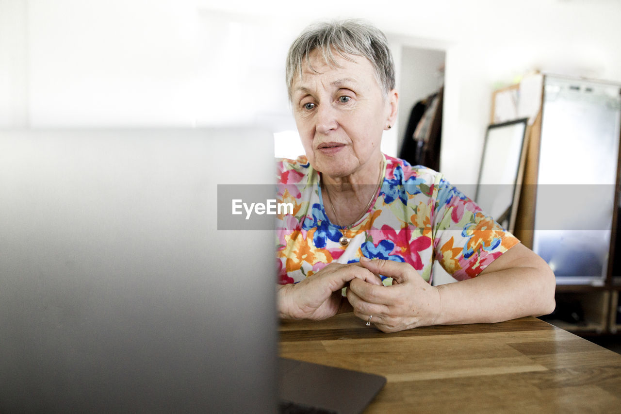 Senior woman sitting at table at home using laptop