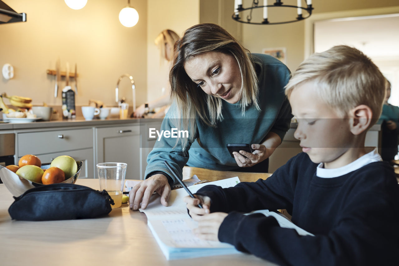 Mother assisting son while doing homework at home