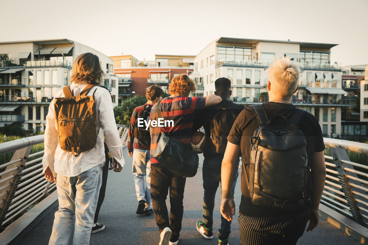 Young and teenage male friends walking on bridge in city