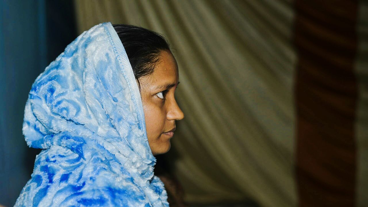 SIDE VIEW OF YOUNG WOMAN AGAINST BLUE WALL