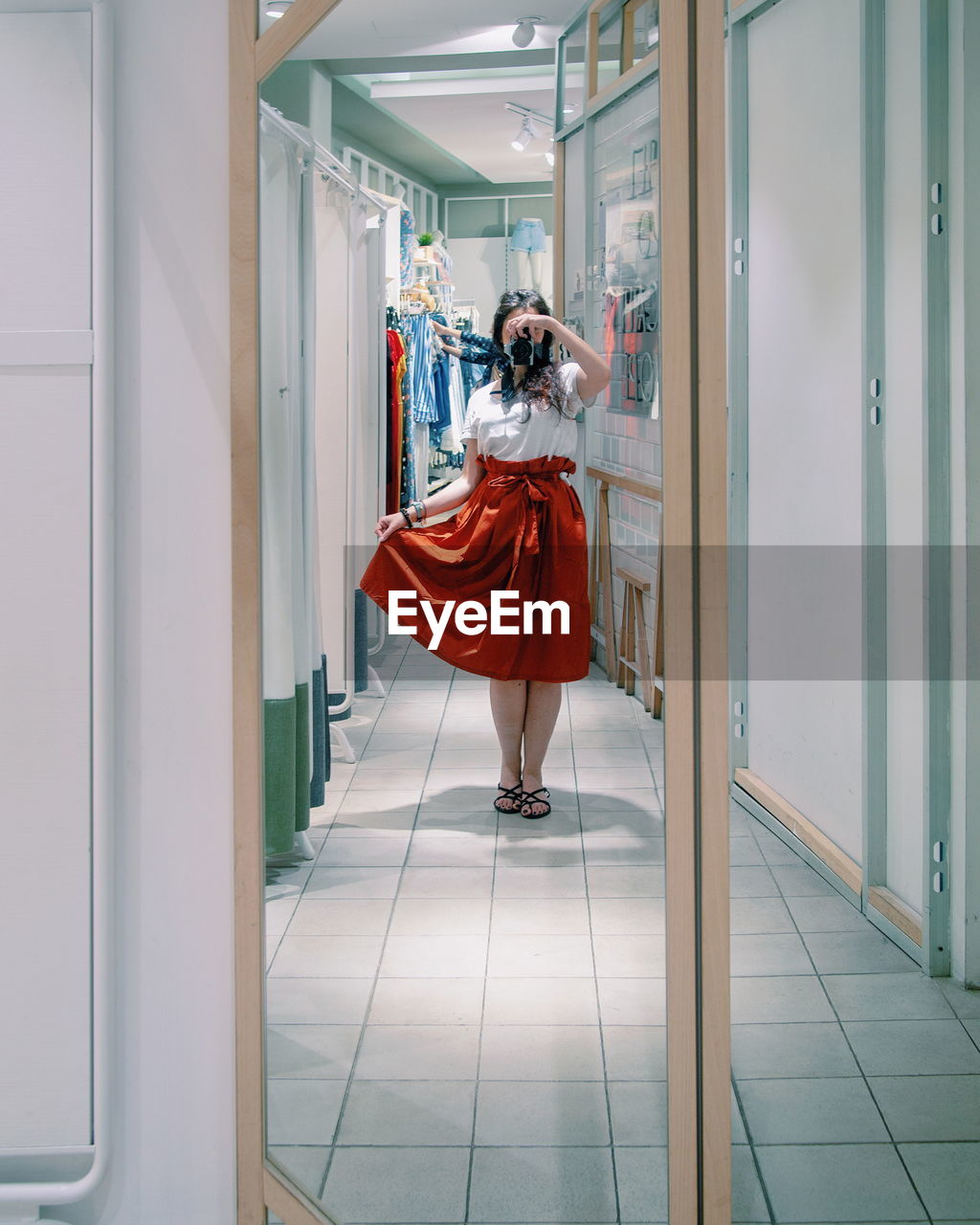 Full length of woman photographing while reflecting on mirror in store