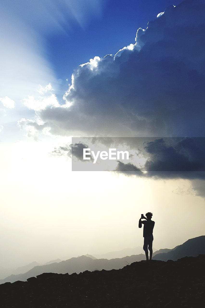 SILHOUETTE MAN STANDING BY MOUNTAIN AGAINST SKY