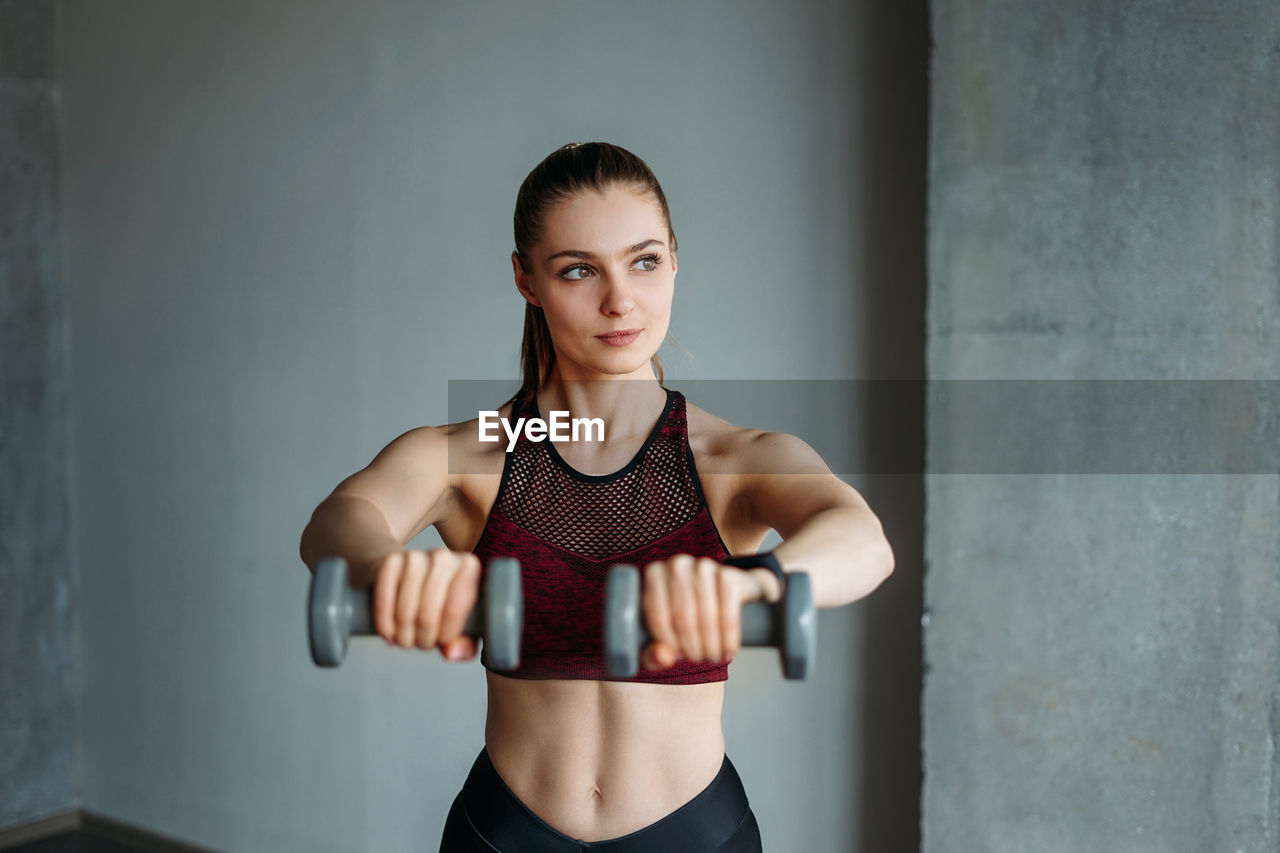 Young woman lifting dumbbells against wall