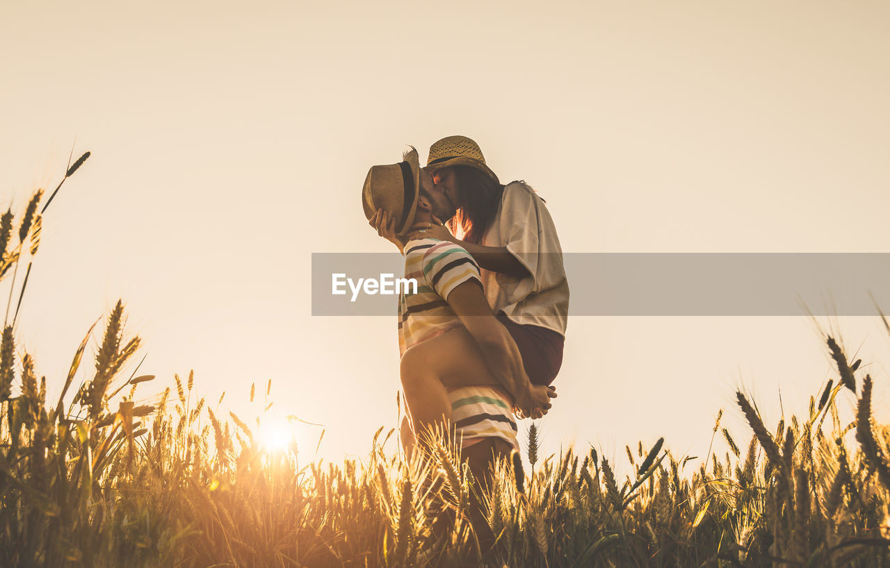 Couple kissing while standing against sky during sunset