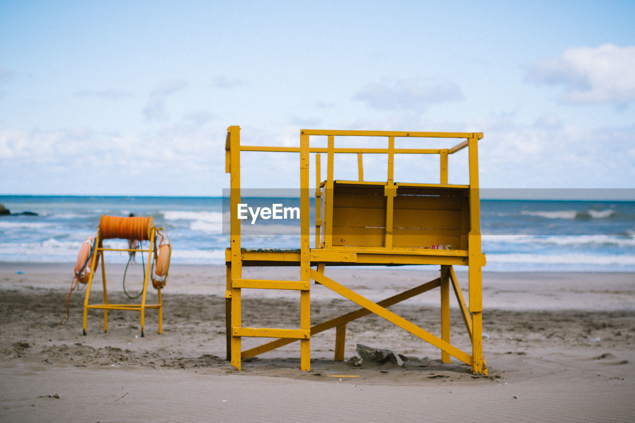 Lifeguard chair on sand at beach against sky