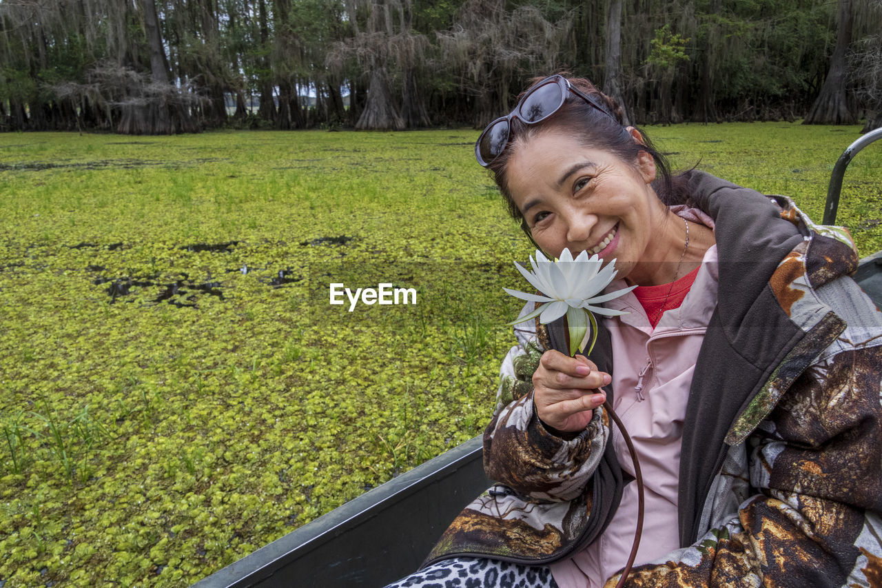 Portrait of smiling senior woman holding flower while sitting on boat