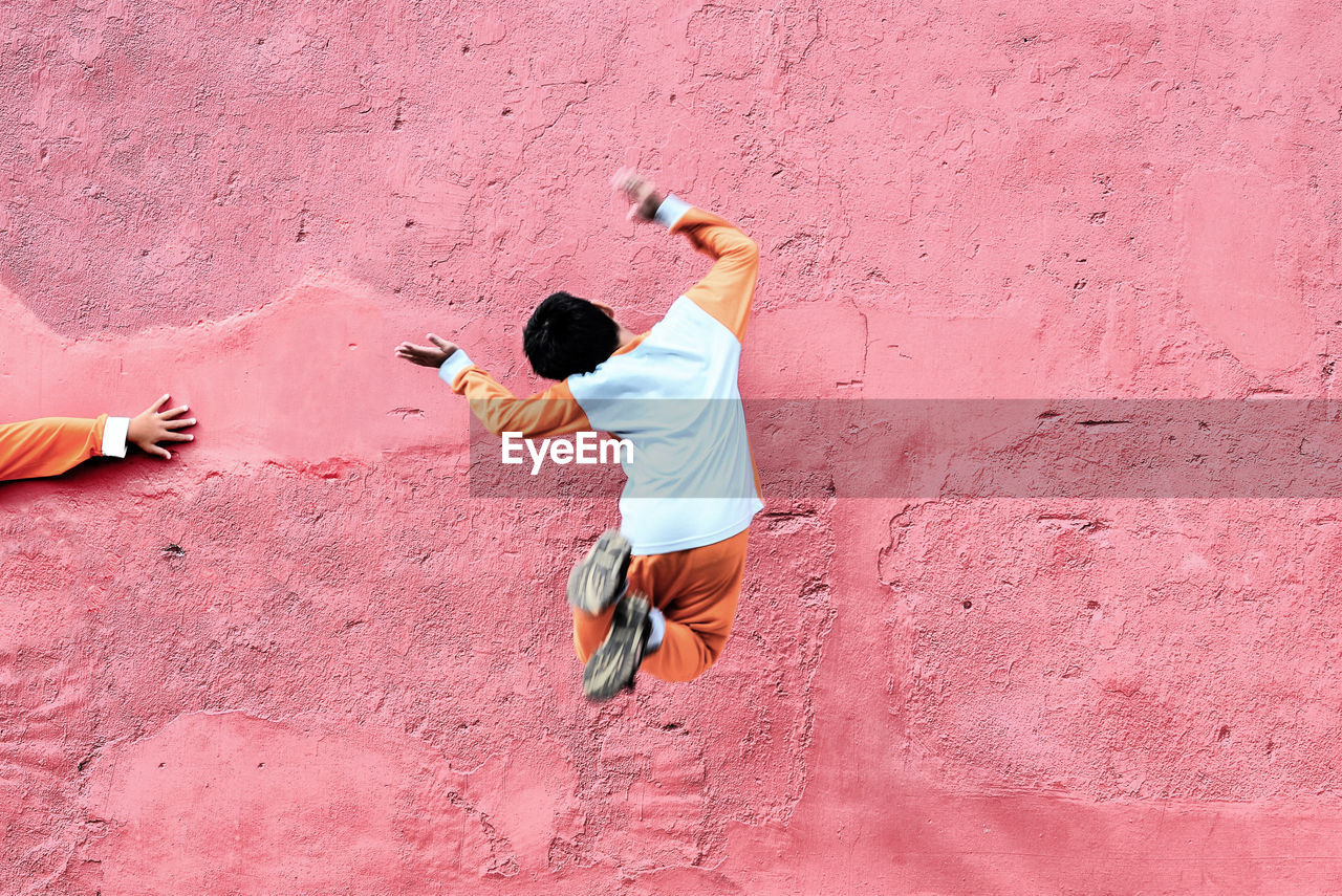 Full length of boy jumping in mid-air against pink wall